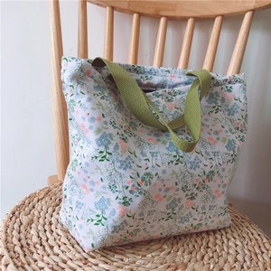 Detailansicht der Blumen-Stofftasche mit grünen Henkeln auf einer Webmatte