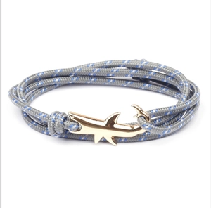 Detail of shark-shaped golden clasp with grey blue-spotted woven rope bracelet