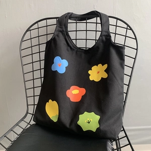 Dettaglio della borsa tote in tela nera con stampa floreale astratta colorata su sedia metallica