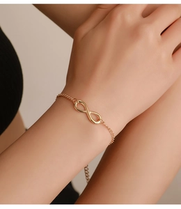 Detail of gold infinity symbol bracelet on wrist showing the fine chain and smooth finish