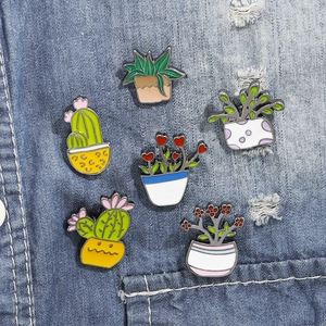 Detailed view of six cactus enamel pins displayed on a denim fabric background