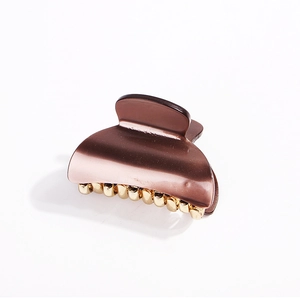 Detail of a brown acrylic claw clip featuring elegant gold metal teeth on a white background