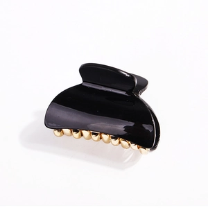 Close-up of minimalist black acrylic claw clip with gold metal teeth on white background