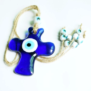 Macro shot of blue glass cross hanging ornament with evil eye charms and natural jute rope