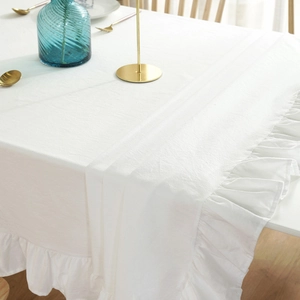 Detail of white cotton linen tablecloth featuring elegant ruffled edges and natural texture