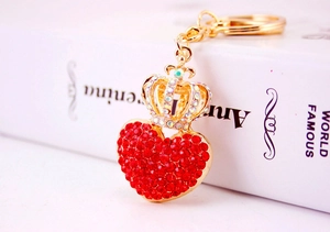 Close-up of gold-tone keychain with sparkling red rhinestone heart and crystal crown charm