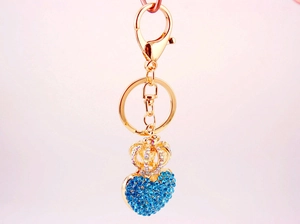 Detail of gold keychain with blue rhinestone heart and crown pendant on pink background