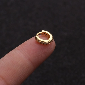Macro shot of a small gold hoop earring with micro-pave zircons held on a fingertip