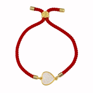 Detalle de una pulsera ajustable de cuerda roja con un colgante de corazón dorado de drusa