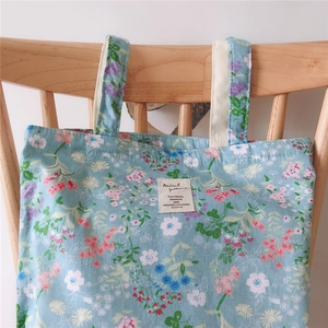 Detail of blue floral canvas tote bag showing textile texture and label on a wooden chair