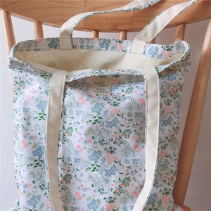 Close-up of floral cotton tote bag texture and brand label on a light wooden seat