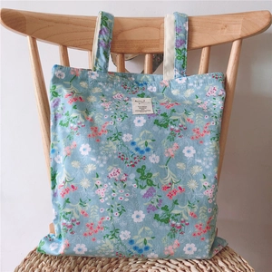 Detail of floral cotton tote bag with light blue millefleurs print hanging on wood chair