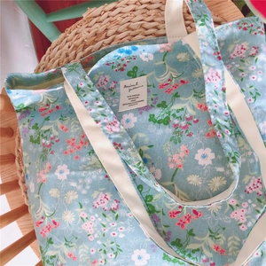 Close-up of floral light blue tote bag with cream straps on a rustic woven stool