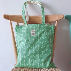 Detail of green canvas tote bag with geometric lines hanging on a wooden chair