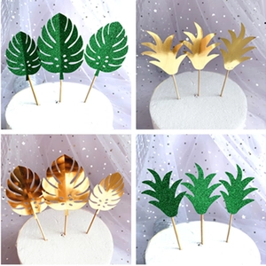 Detail of laser-cut gold and green acrylic tropical leaf toppers for cake decoration