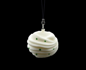 Detail of cream swirl puff keychain with green dots and silver lobster clasp on black background