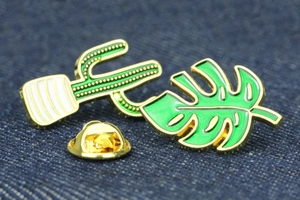 Vue macro détaillée de broches émaillées cactus et monstera sur tissu denim bleu