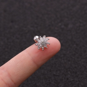 Macro shot of silver sunflower ear stud with clear zircons on a finger tip for size detail