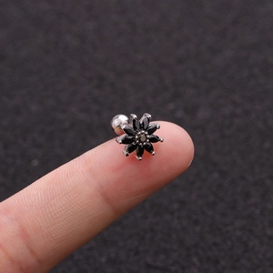 Macro shot of a tiny sunflower-shaped ear stud with black zircon on a fingertip