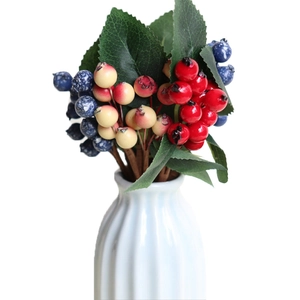 Artificial berry bouquet with red yellow and blue fruits in a white ceramic vase