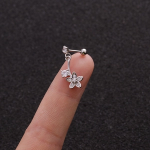 Macro shot of a silver floral piercing stud with cubic zirconia held on a fingertip