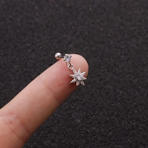 Macro view of silver stainless steel star earring with pavé zircons held on a finger