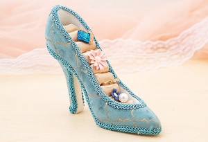 Detail of blue velvet high heel ring holder with gold trim and ring storage slots