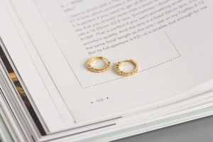 Detailed macro view of gold huggie earrings with crystals set on an open book page