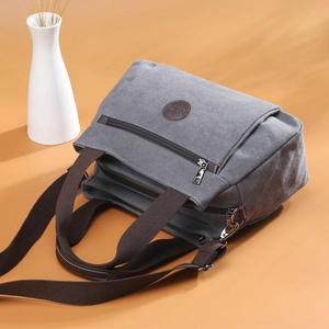 Gray canvas multi-compartment tote bag with brown straps and logo from a 45-degree angle