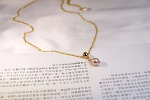 Detailed close-up of a teardrop purple pearl pendant on a gold titanium steel chain
