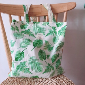Detail of floral canvas tote bag with tropical leaf print and woven label on a chair