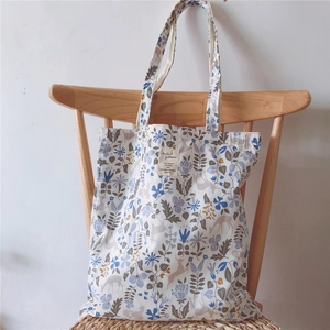 Detail of floral tote bag with reindeer pattern hanging on a rustic wooden chair