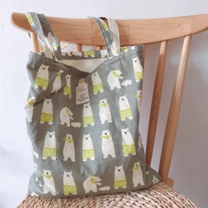 Detail of grey canvas tote bag featuring repeated cartoon polar bear prints and a woven tag
