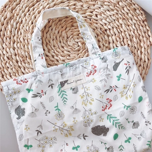 Detail of white cotton tote bag featuring squirrel and bird patterns on a woven mat