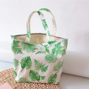 Detail of white canvas tote bag featuring green tropical leaf prints and zipper closure