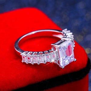 Elegant emerald cut zircon ring in silver finish with pavé side stones on red velvet box