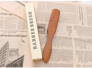 Detail of wooden barber brush with natural bristles next to its paper packaging box