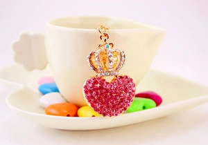 Close-up of golden heart and crown keychain with pink rhinestones on a white plate