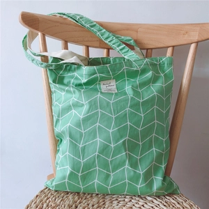 Detail of green herringbone canvas tote bag hanging on a chair with woven cushion