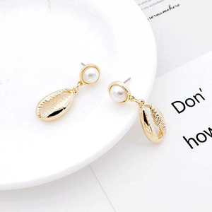 Detailed macro view of golden conch shell earrings featuring round white pearls