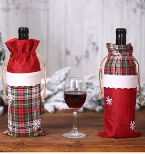 Détail de housses de bouteille de vin de Noël en lin avec motifs à carreaux rouges sur bois