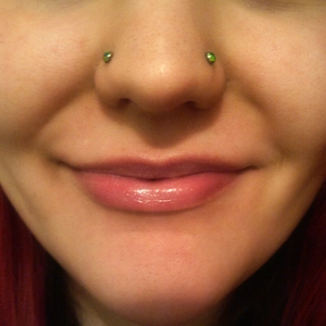 Close-up of iridescent opal labret studs worn as nostril piercings on a model