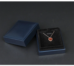Detail of a dark blue jewelry box with a rose gold heart necklace on black velvet