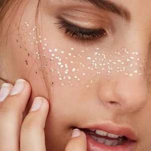Detailed view of golden glitter freckles and metallic makeup sequins on female face