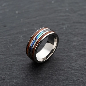 Macro shot of titanium steel ring with wood grain inlay and colorful shell on stone base