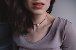 Detail of elegant black leather cord necklace with large white pearl and matching earrings