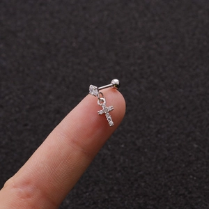 Macro shot of silver stainless steel earring with micro zircon cross pendant on a finger
