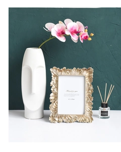 Close-up of golden vintage relief photo frame with orchid and ceramic vase decor