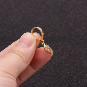 Close-up of golden huggie hoop earring featuring a feather pendant with clear zircon stones