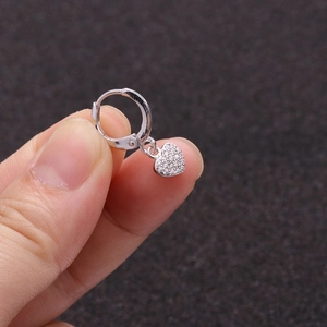 Close-up of a silver hoop earring with a sparkling heart pendant held by hand